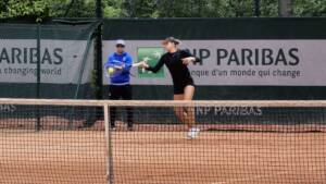 Professional tennis player hitting a forehand stroke with coach watching on